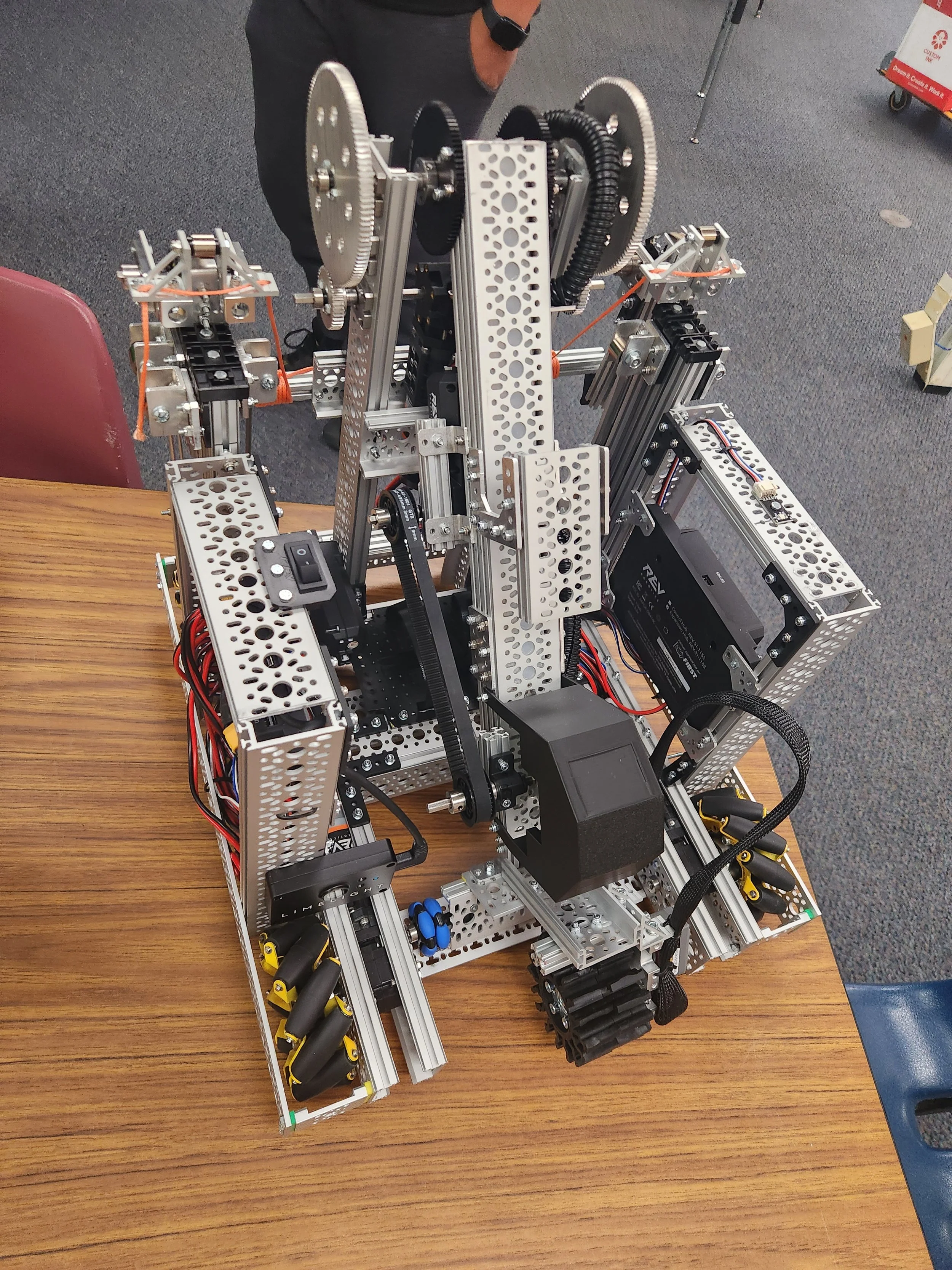 A complex metal robotic machine with gears, wires, and electronic components on a wooden table.
