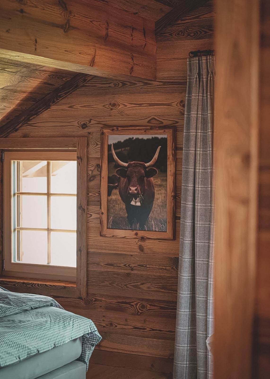Une chambre en bois avec une fenêtre et un tableau représentant un taureau dans la nature.