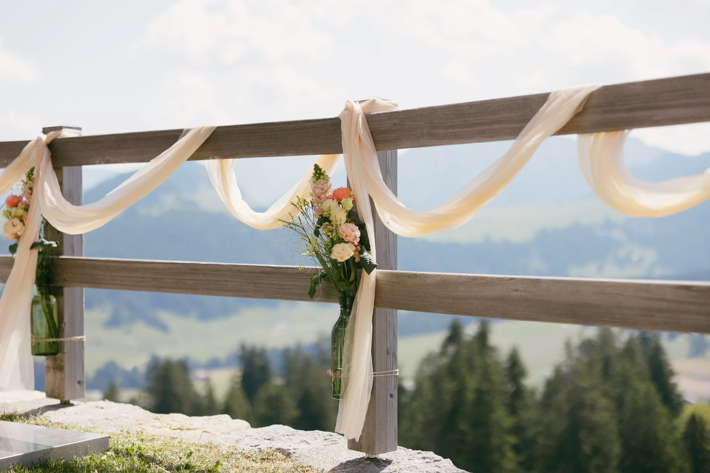 Décoration de mariage avec des drapés et un bouquet de fleurs accroché à une clôture en bois dans un cadre naturel