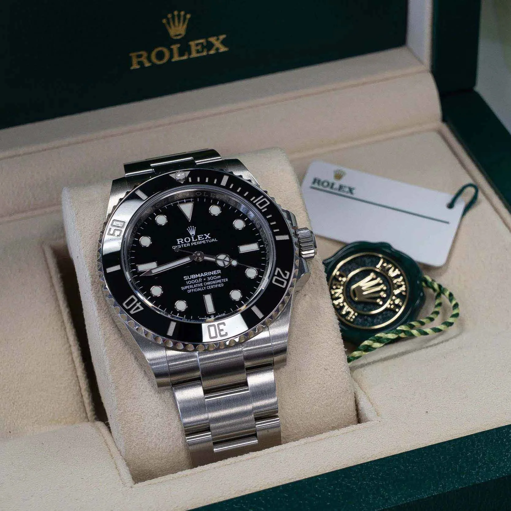 A Rolex Submariner wristwatch with a black dial and a stainless steel bracelet, displayed in a beige watch box with the Rolex logo and a tag with the Rolex logo and branding.
