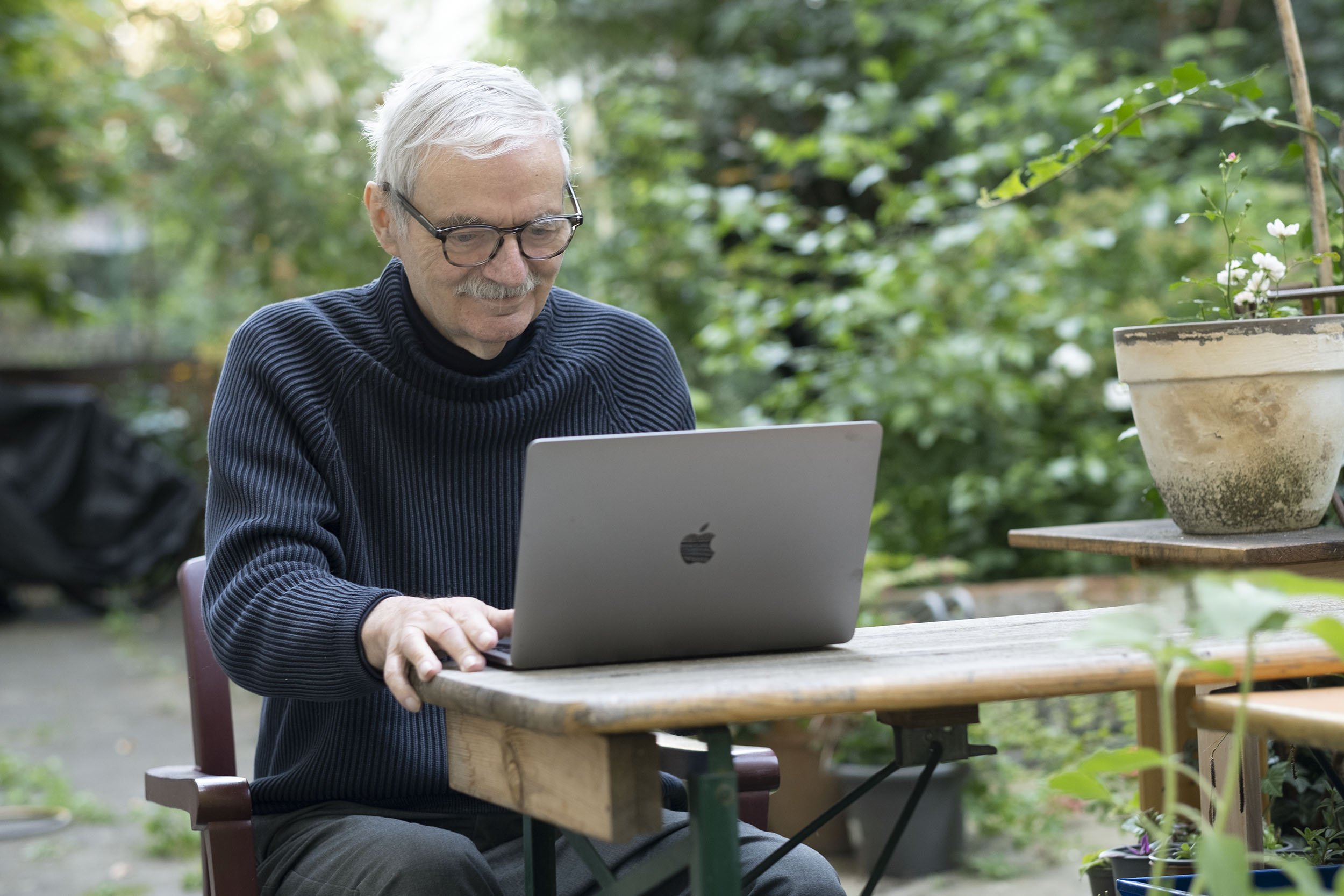Udo Baer arbeitet an einem Laptop im Grünen auf einer Terrasse.