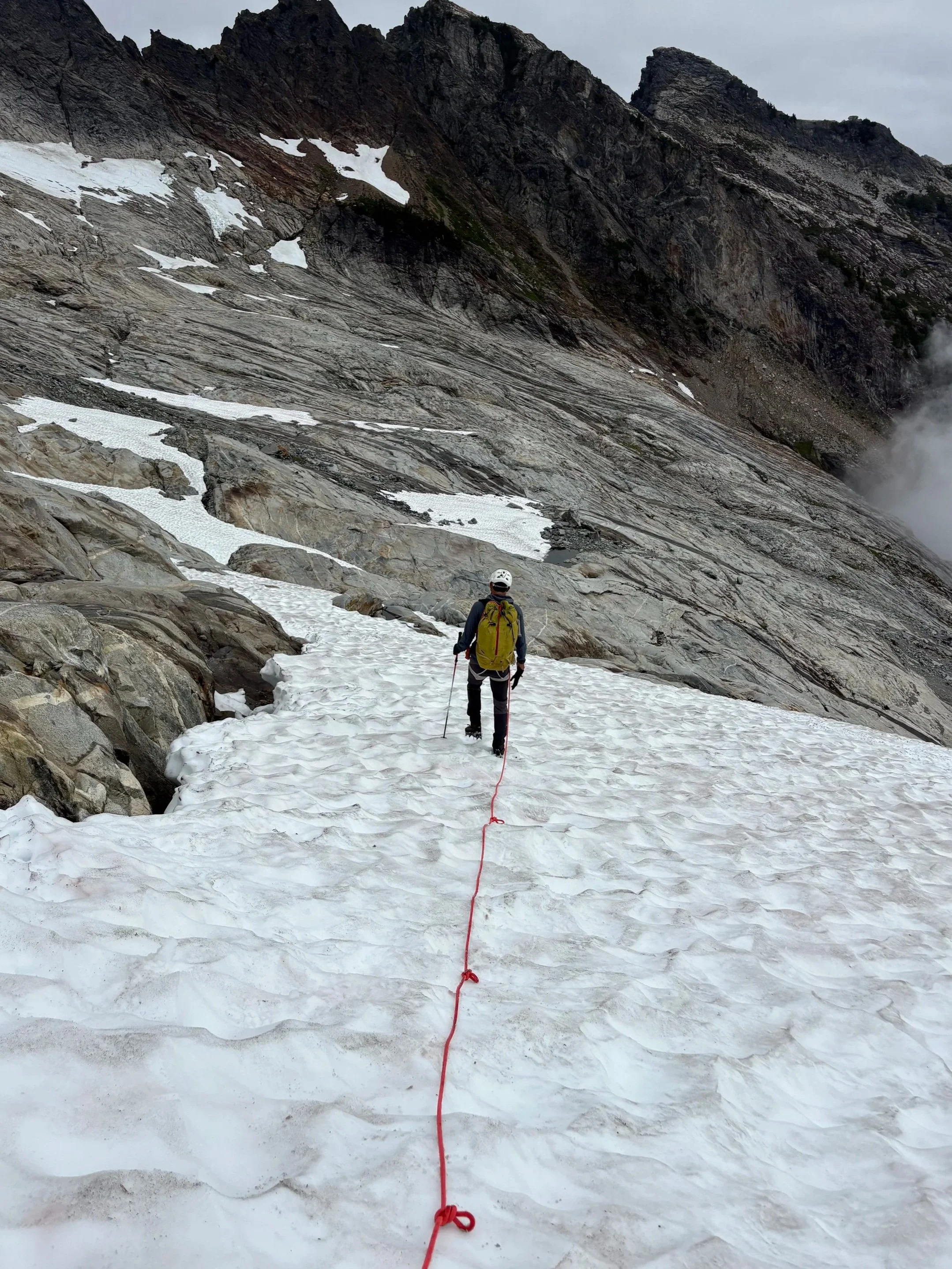 Solitary man walking along a glacier with a rope behind him