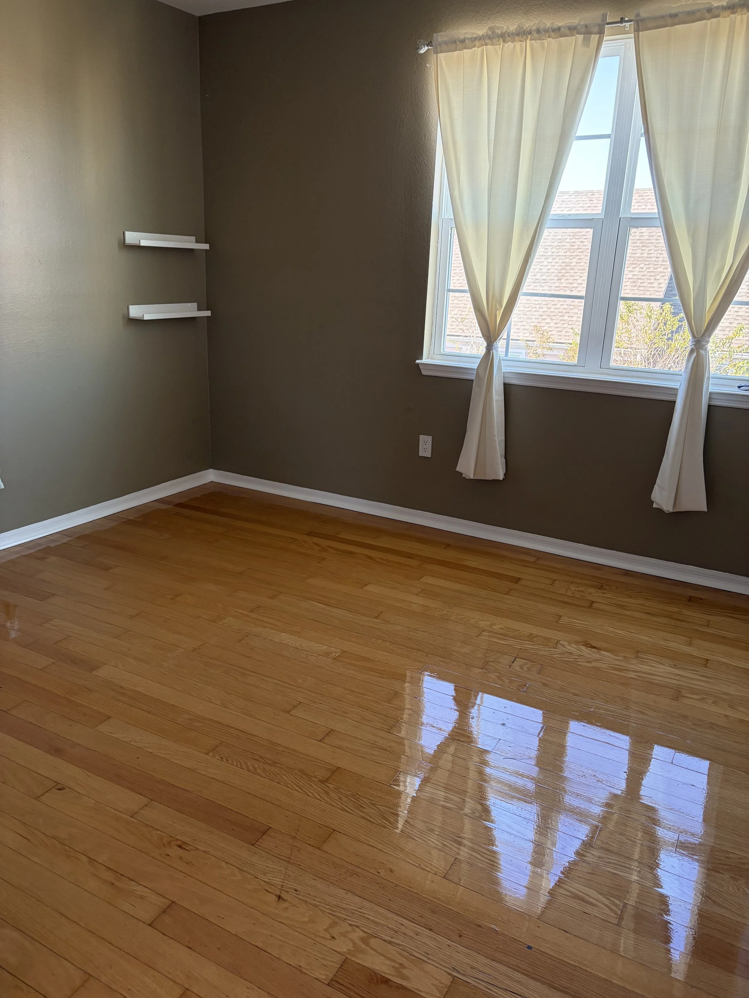 A clean room with olive colored walls, white curtains, and shiny brown wooden floors