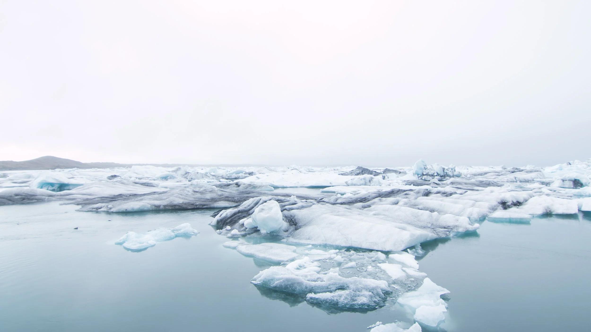 Paysage glaciaire avec des morceaux de glace flottant dans l'eau, ciel nuageux très clair.