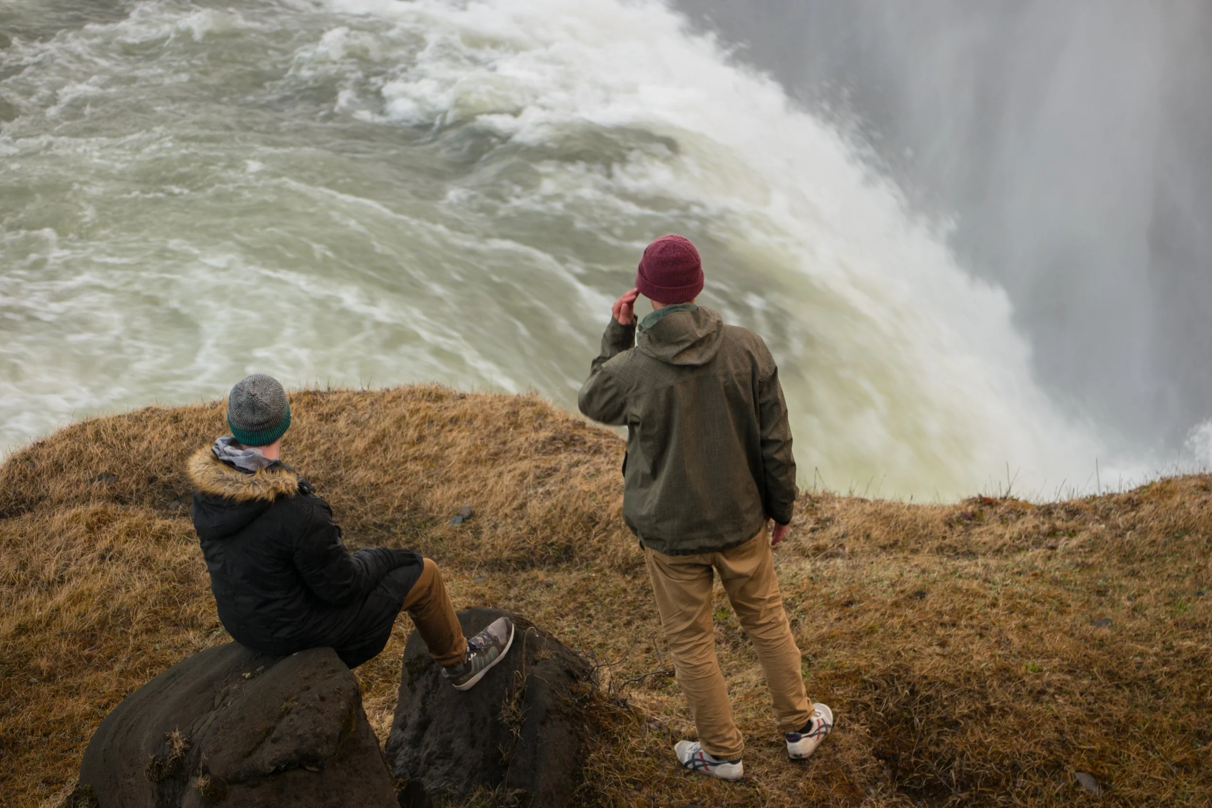 Deux personnes observant une chute d'eau depuis un rivage rocheux et herbeux.