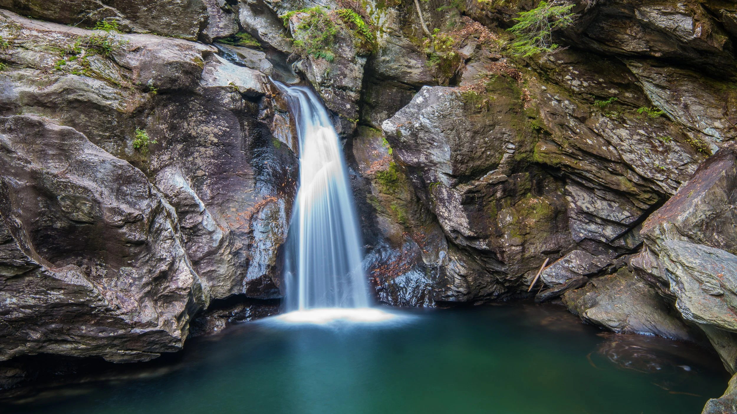 Petite cascade dans une gorge rocheuse avec de l'eau claire coulant sur des rochers.