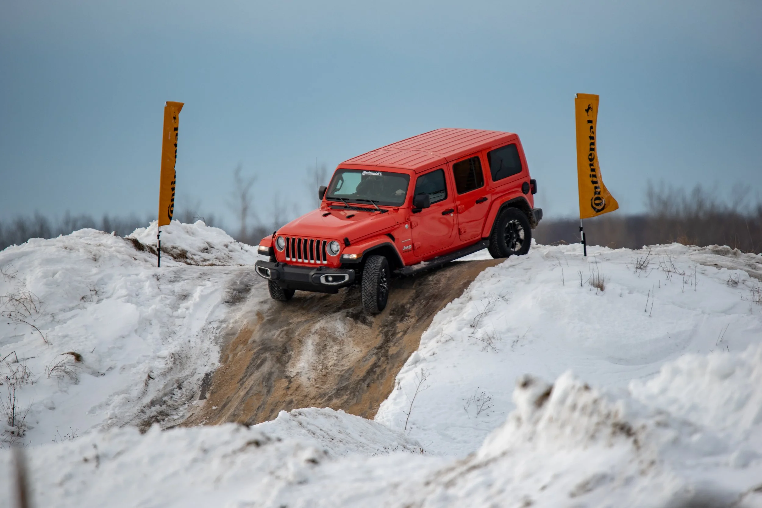 Un véhicule tout-terrain rouge traverse un terrain enneigé, avec des drapeaux orange aux extrémités du chemin.