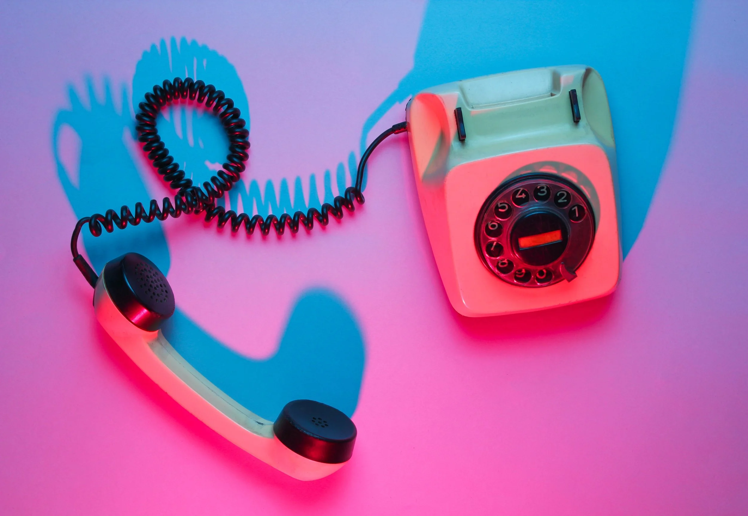 Retro rotary dial phone connected to a wall with a bright pink and blue lighting effect.