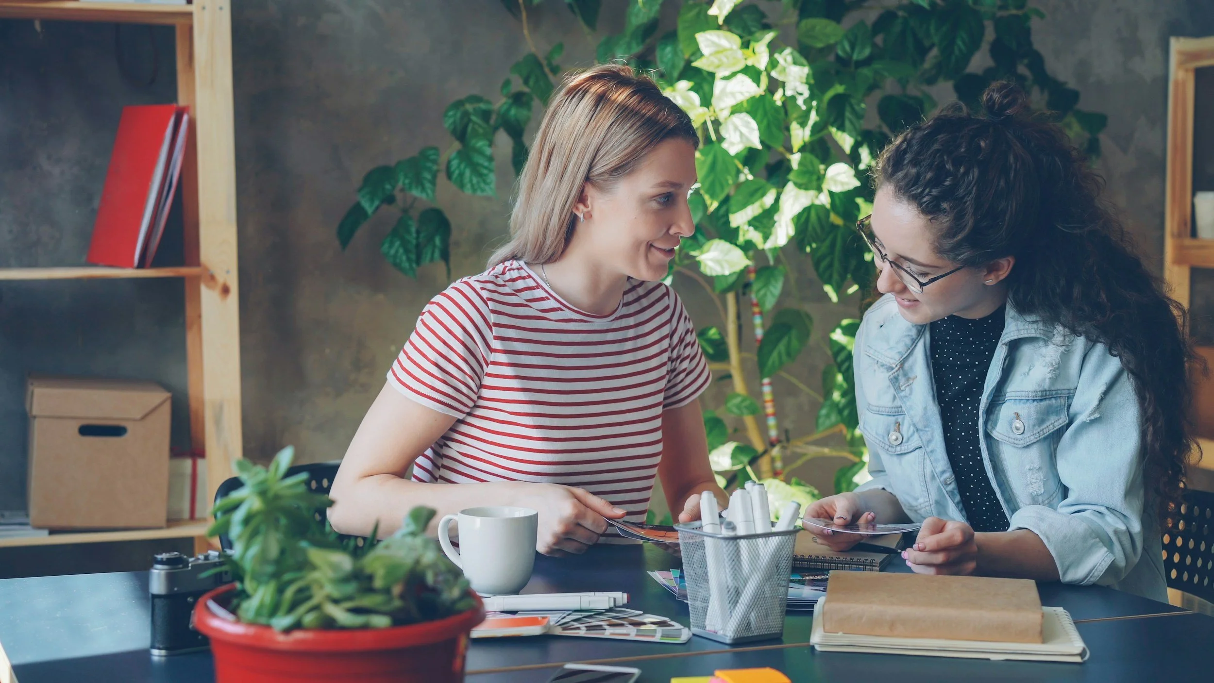 A warm, professional photo of two women talking across a small table with a notebook and coffee