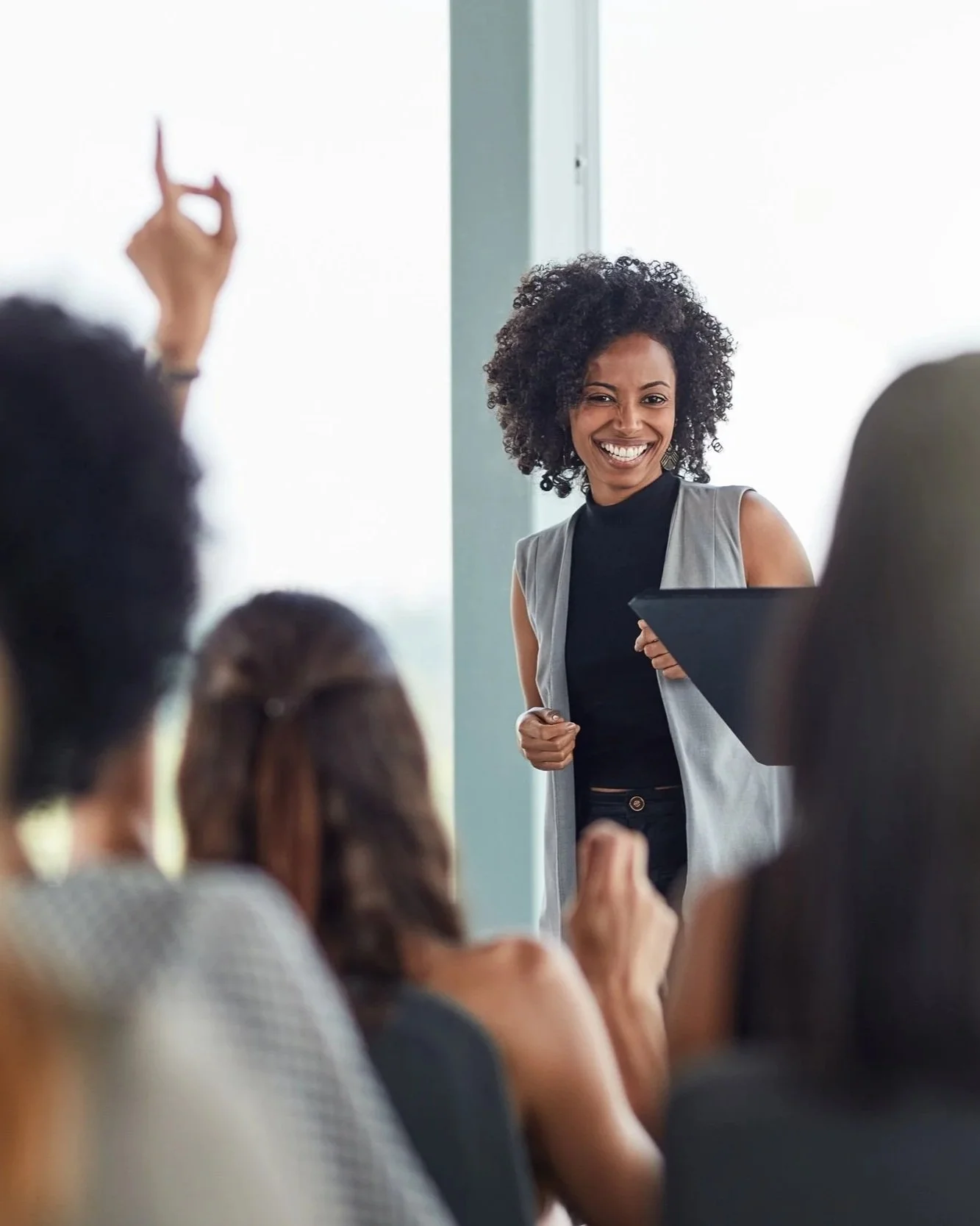 A woman with curly hair smiling while speaking to a group of people in a meeting room.