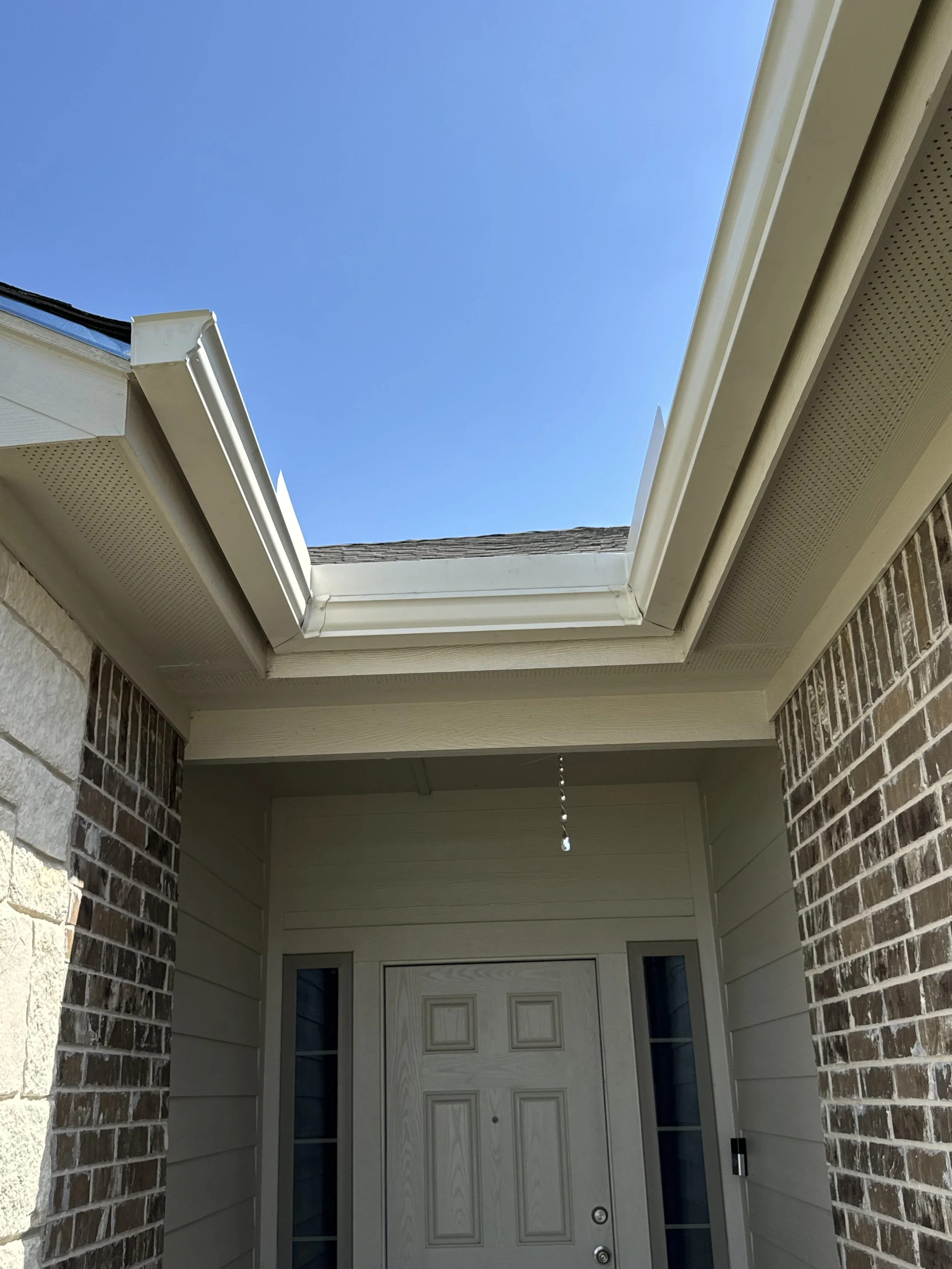 View of a house entryway with a door, brick and siding walls, and an open skylight with a blue sky visible.
