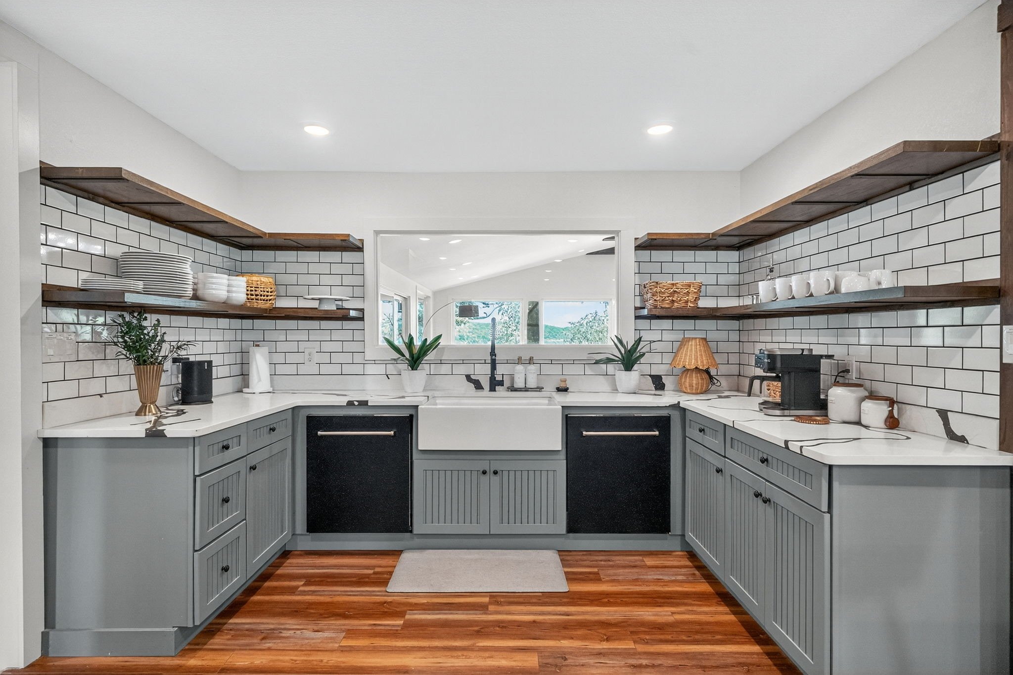 Modern farmhouse-styled kitchen with white subway tile backsplash, open wooden shelves, gray lower cabinets, black accents, and wood flooring.