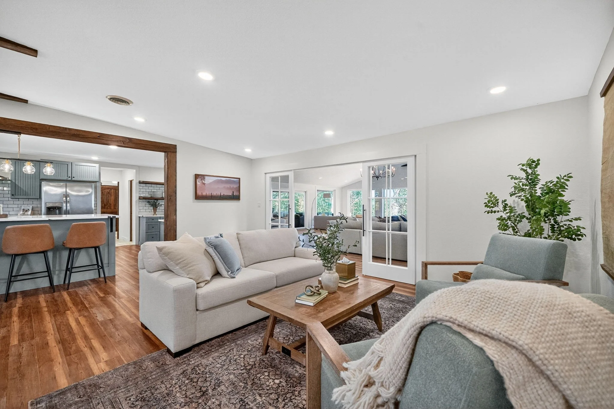 Sitting room with a sleeper sofa, blue armchairs, wooden coffee table, greenery and sliding glass doors leading to the spacious Great Room.