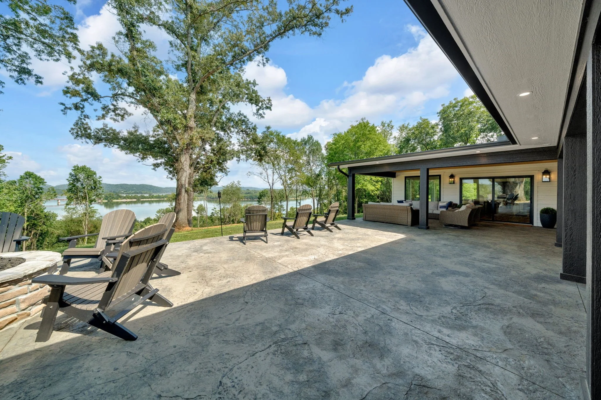 Spacious outdoor patio with view of trees and lake, furnished with multiple chairs and sofas - perfect to hosting events.