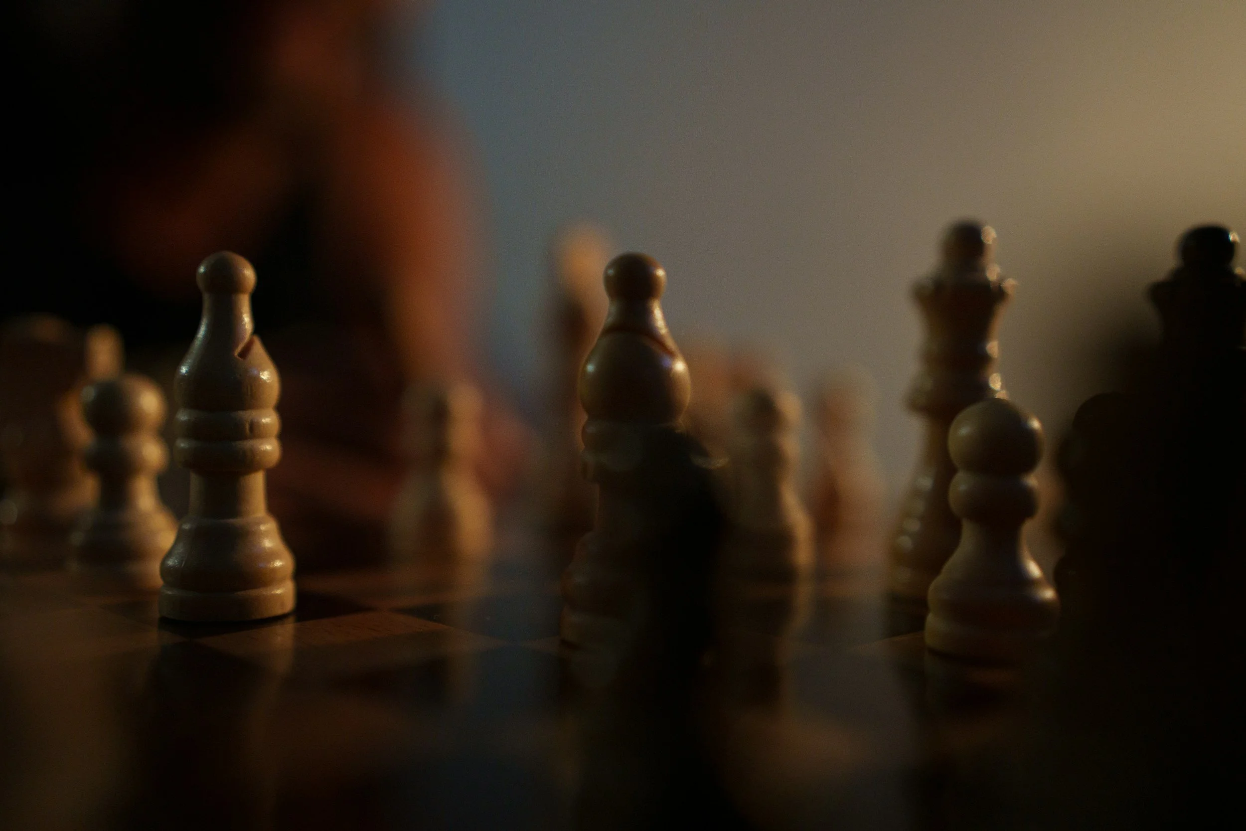 Close-up of wooden chess pieces on a chessboard, with a dark background and subdued lighting.