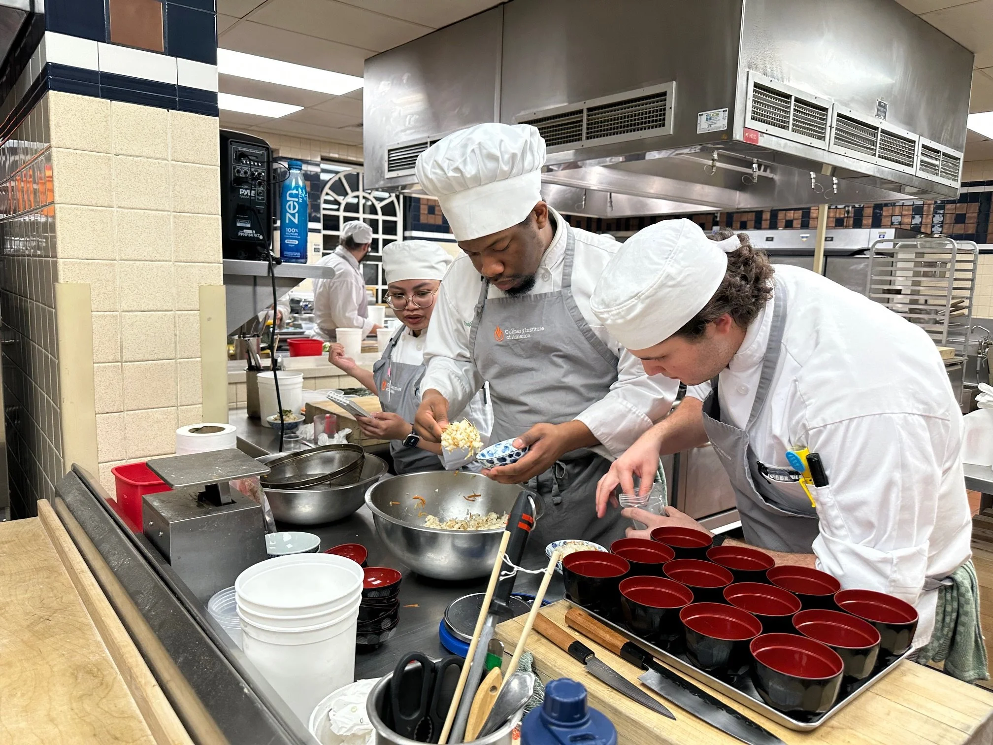 A group of chefs in a restaurant kitchen preparing food and filling bowls with ingredients.