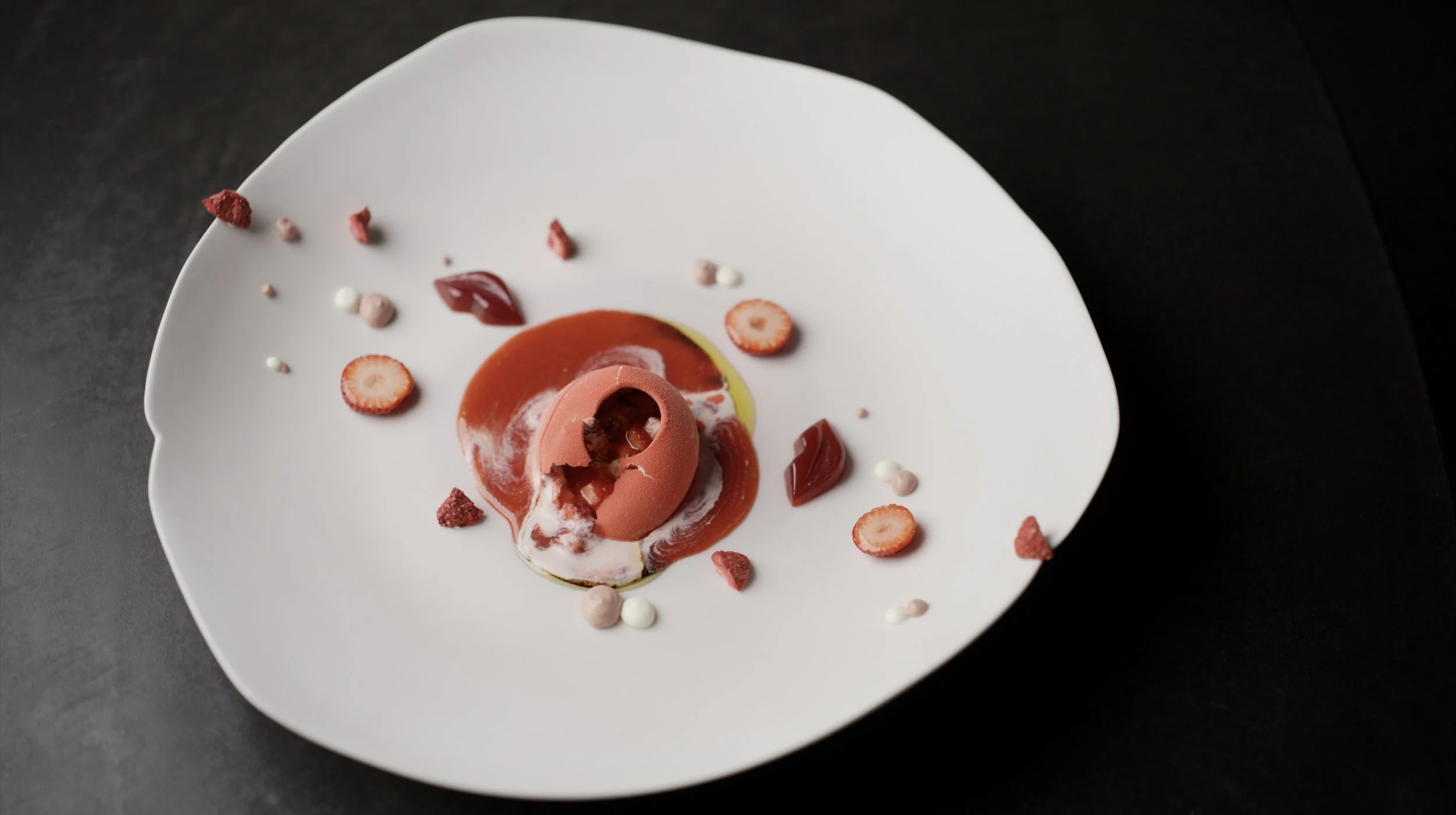Elegant dessert on a white plate with red sauce, pink cream, strawberry slices, and small decorative edible elements.