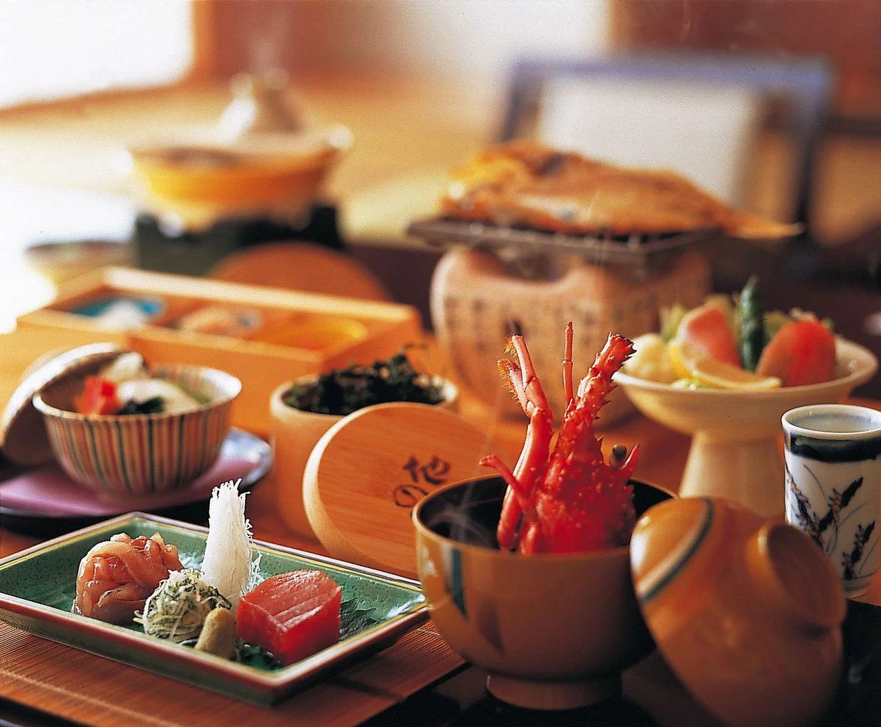 A Japanese meal spread with various dishes including sashimi, cooked seafood, and side dishes in bowls and plates on a wooden table.