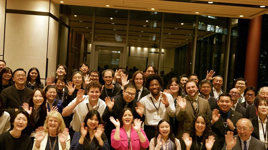 Group of people smiling and waving at a gathering or event indoors.