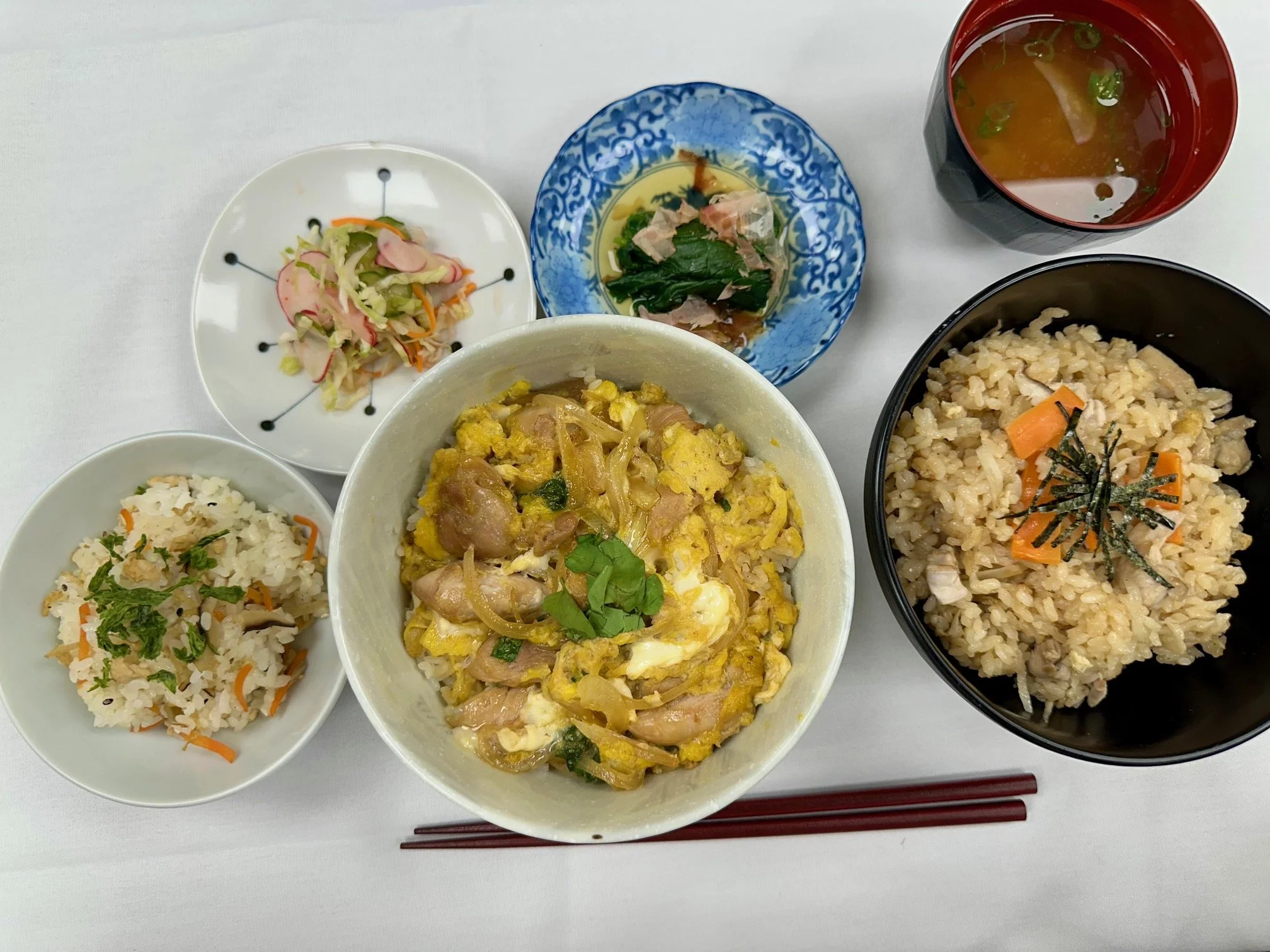 Japanese meal with rice, egg and chicken in a bowl, rice with vegetables and seaweed, pickled vegetables, salad, miso soup, and green onion soup