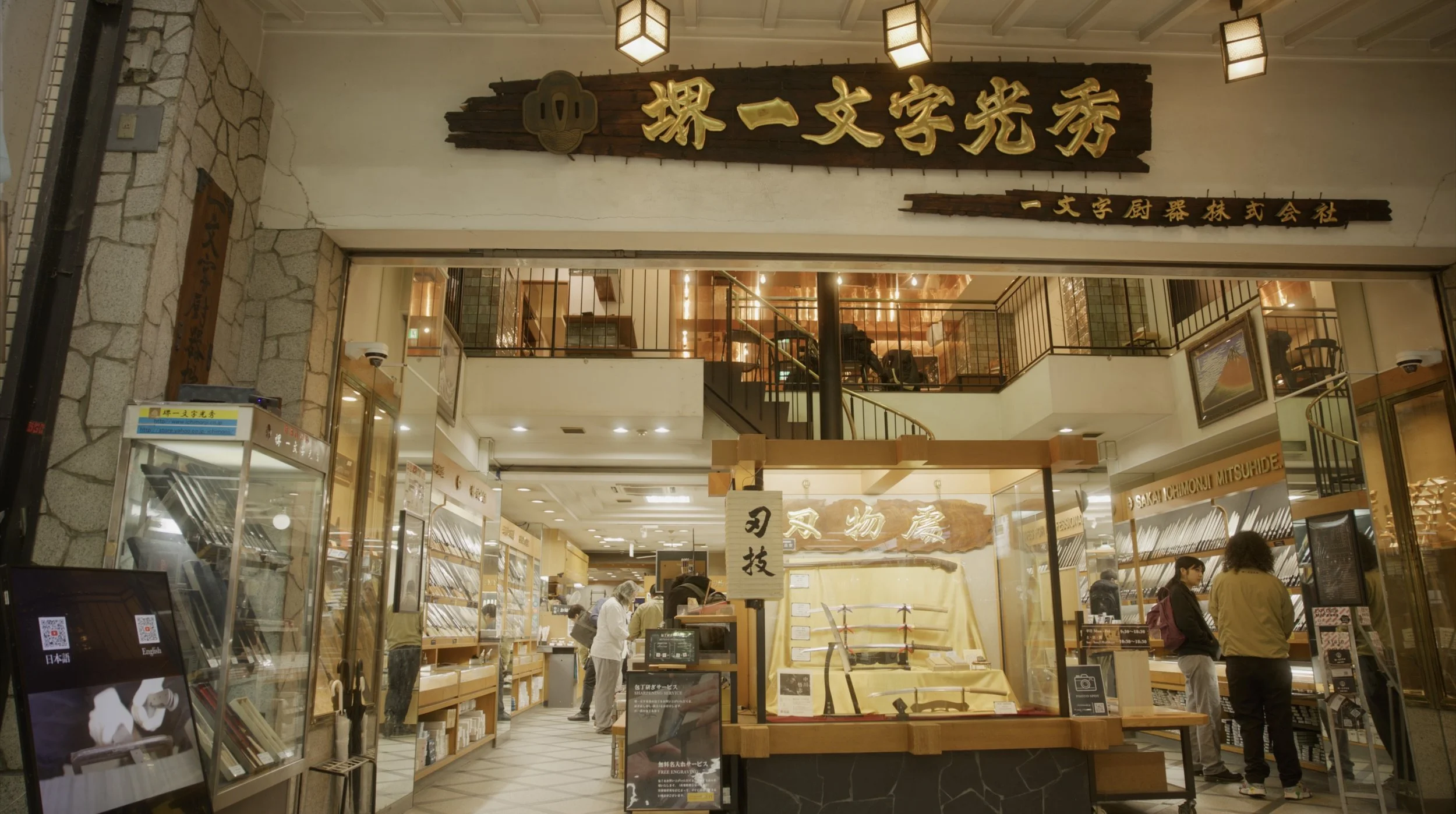 Inside a store with Japanese swords on display, people browsing, and signs in Japanese.