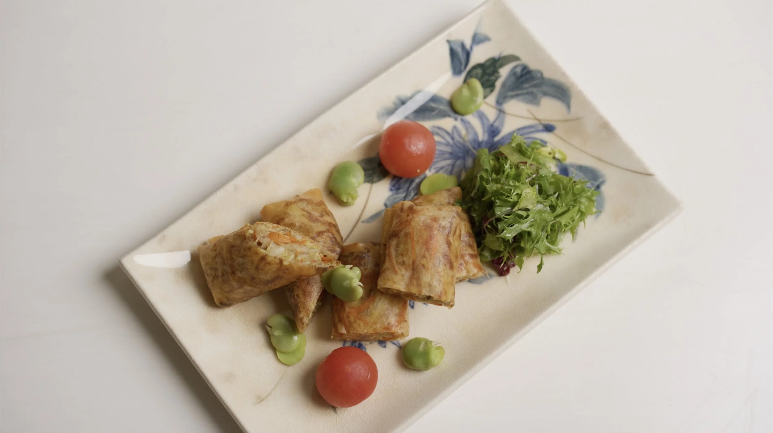 Plate with spring rolls, cherry tomatoes, green peas, and leafy greens on a decorative ceramic dish
