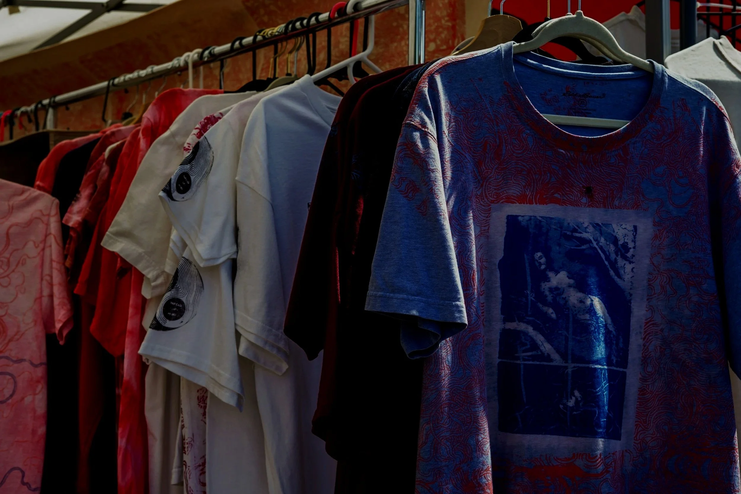 A row of hanging T-shirts on a clothing rack, featuring various colors and designs, including a prominent blue T-shirt with a graphic print.