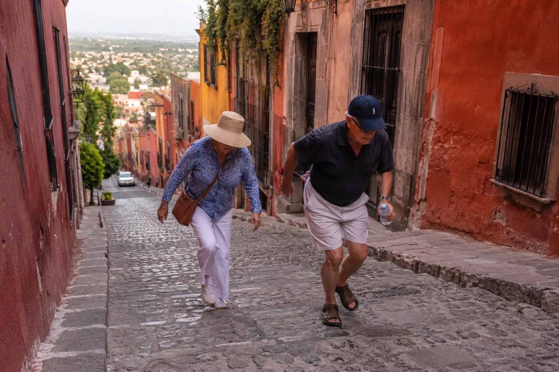 Older couple walking up a steep cobblestone hill in San Miguel de Allende on a warm afternoon.