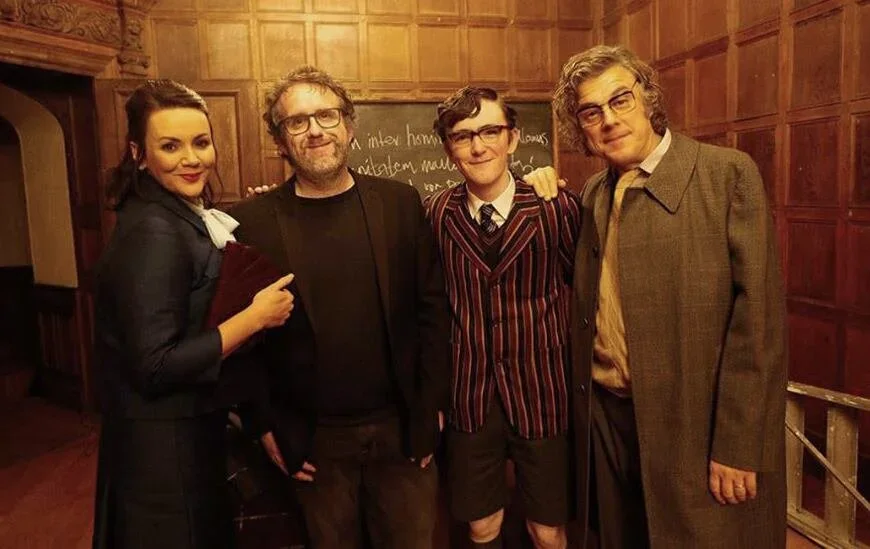 Four people dressed in vintage-style clothing standing together in a wood-paneled room, posing for a photo.
