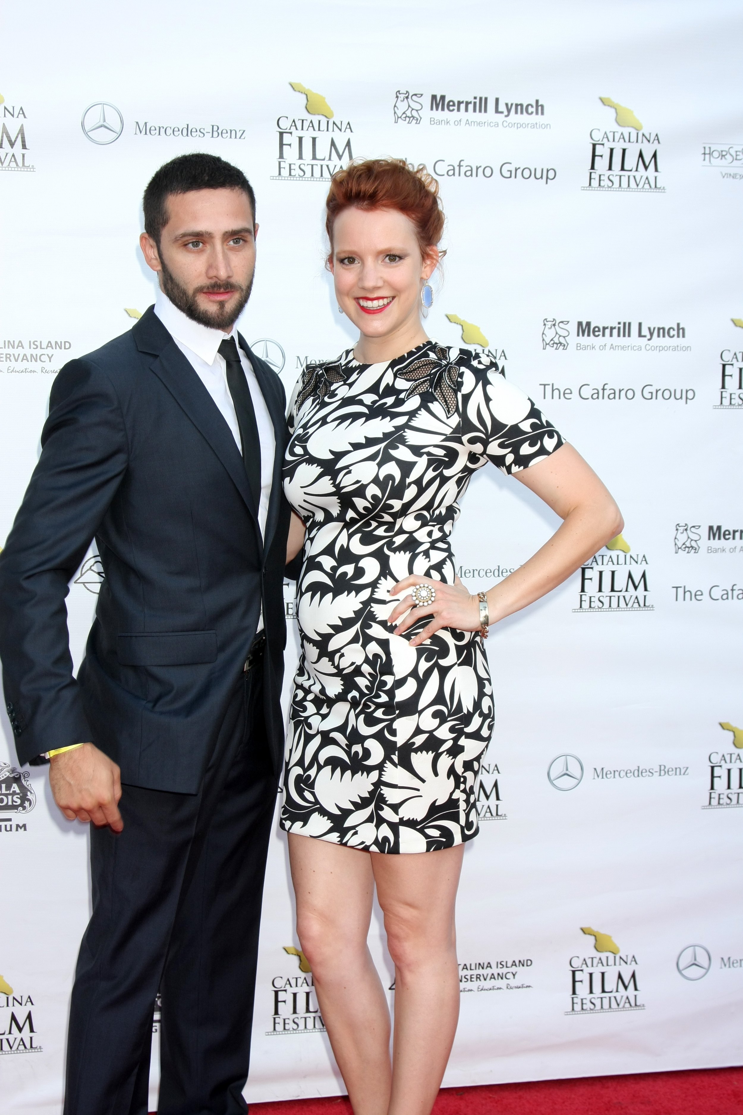 A man and woman posing on the red carpet at the Catalina Film Festival. The man is wearing a dark suit and tie, and the woman is wearing a black and white patterned dress with jewelry.