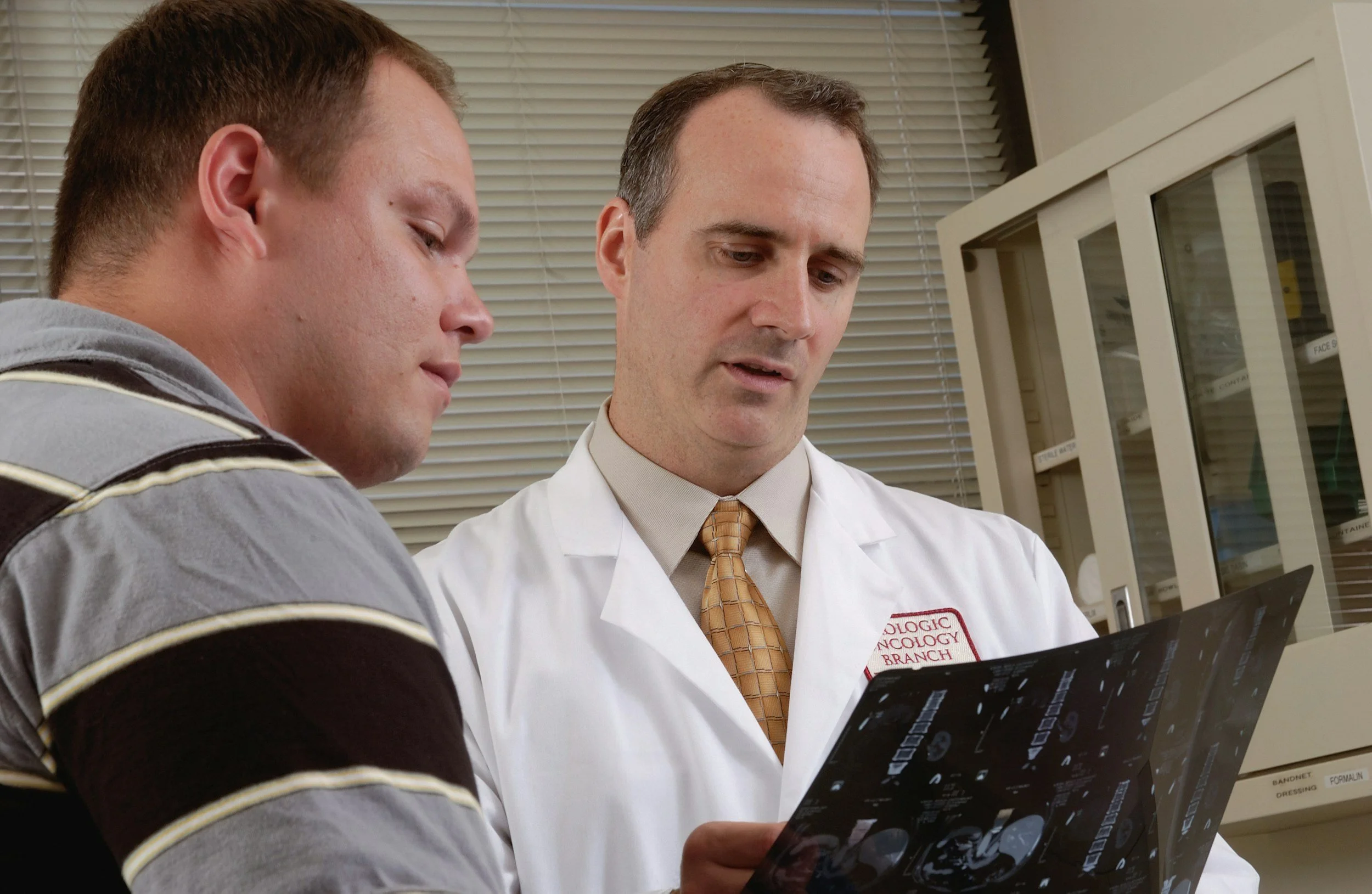 A doctor showing an X-ray film to a young male patient in a medical office.