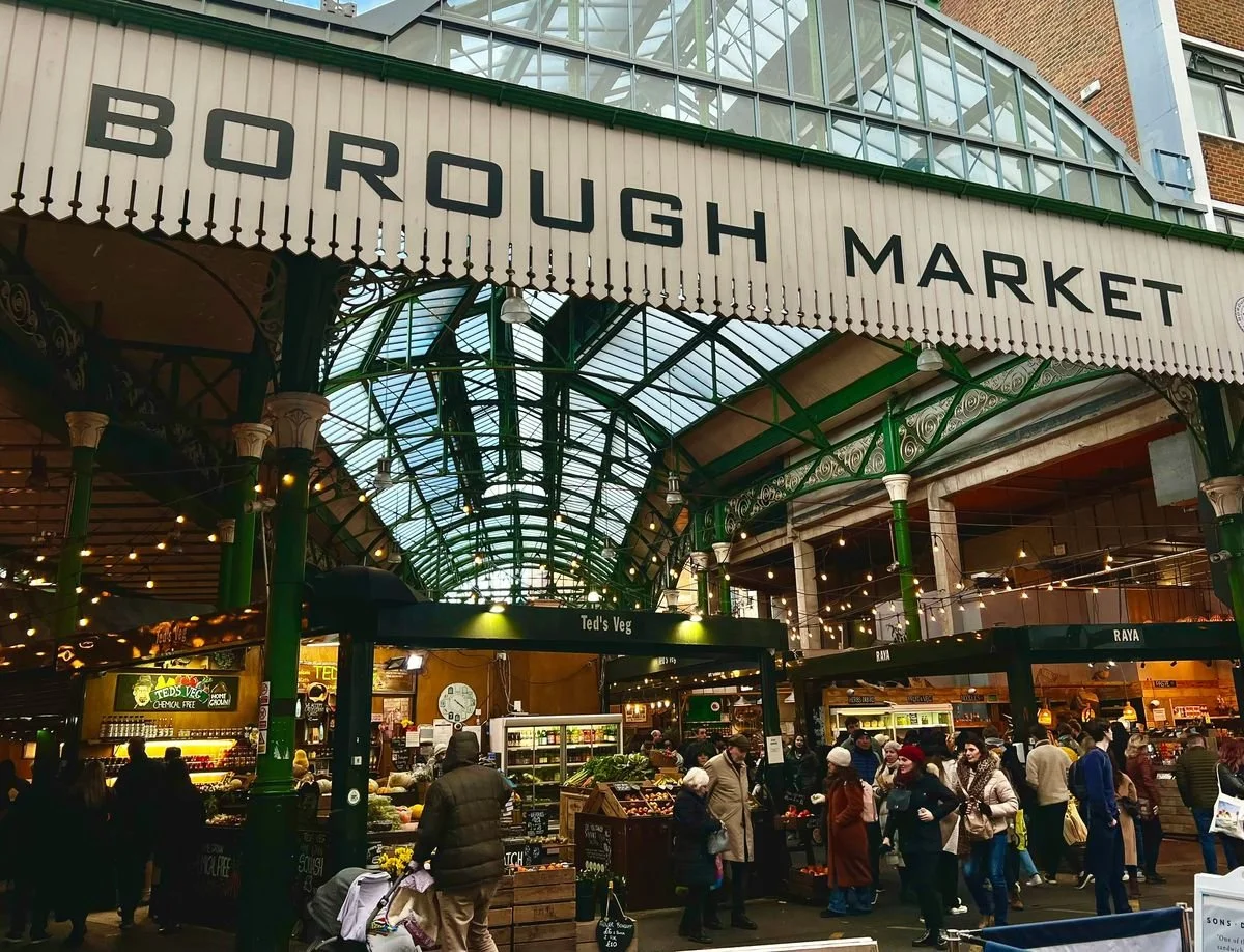 People shopping at Borough Market with a large sign overhead and an indoor market area with food stalls.