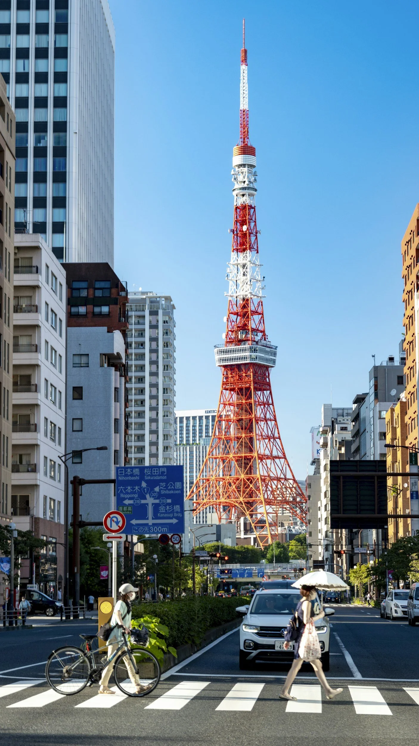 Tokyo Tower towering over busy city street with pedestrians, cars, and bicycles, under clear blue sky.