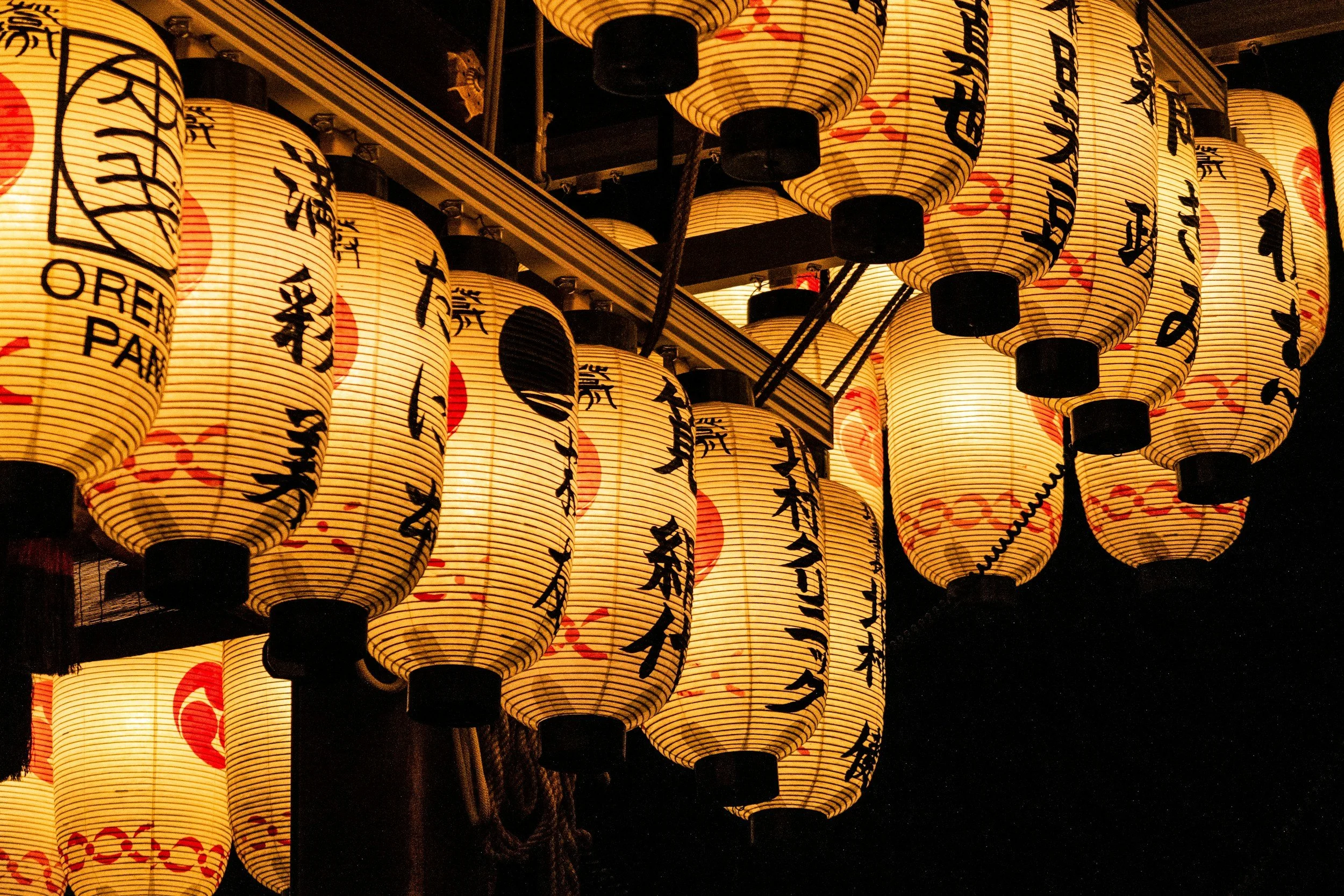 Multiple traditional Japanese paper lanterns hanging at night, decorated with black Japanese characters and red symbols.