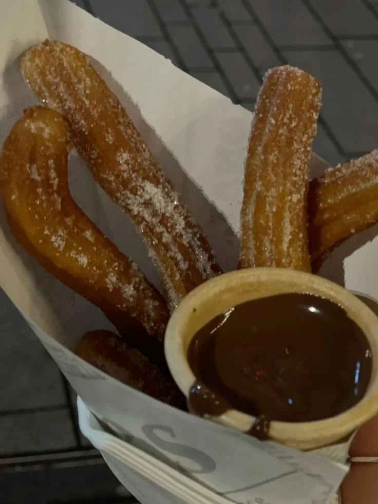 Churros covered in sugar served with a cup of chocolate sauce for dipping.
