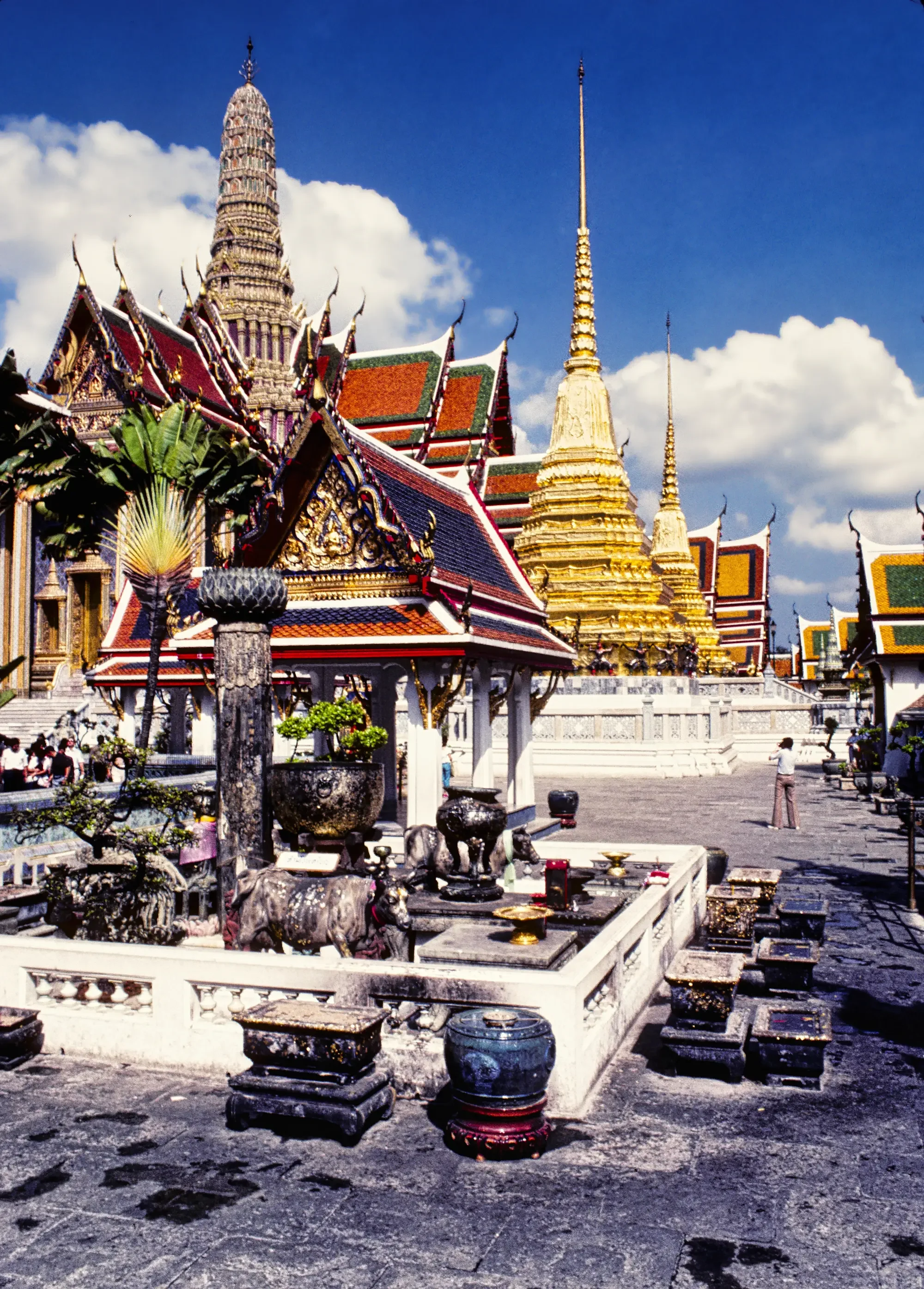 Colorful Thai temple with ornate rooftops and golden pagoda against blue sky with white clouds.