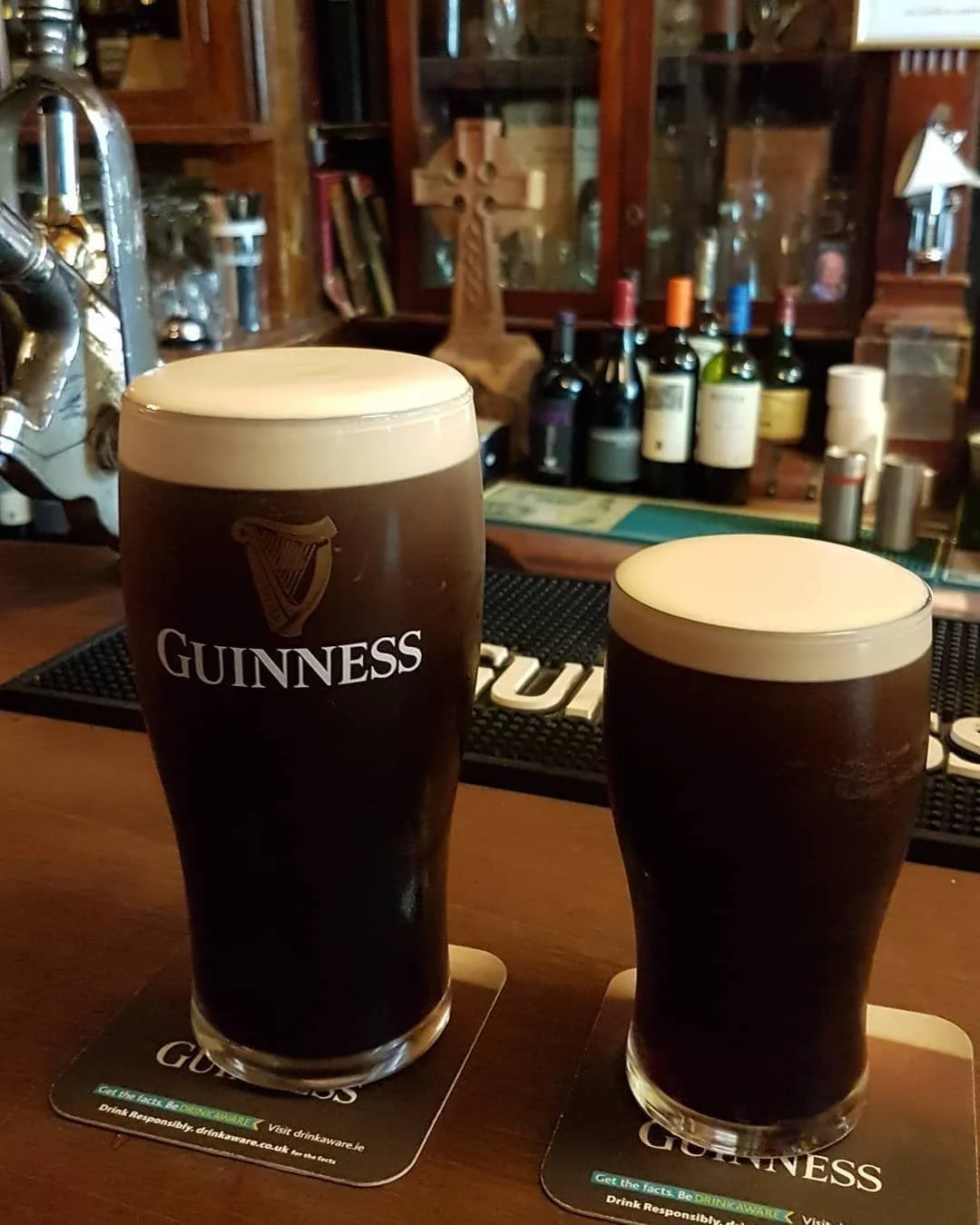 Two pints of Guinness beer with frothy heads on coasters on a bar counter.