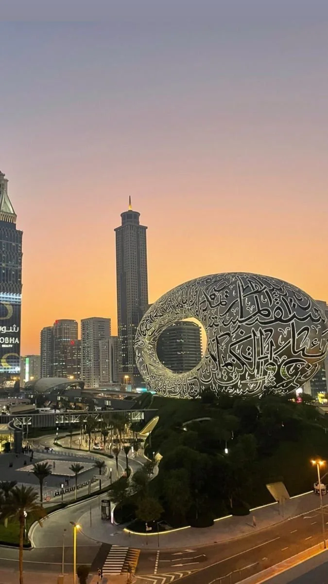 Cityscape of Dubai at sunset featuring the Dubai Frame and the Museum of the Future building with Arabic calligraphy design.