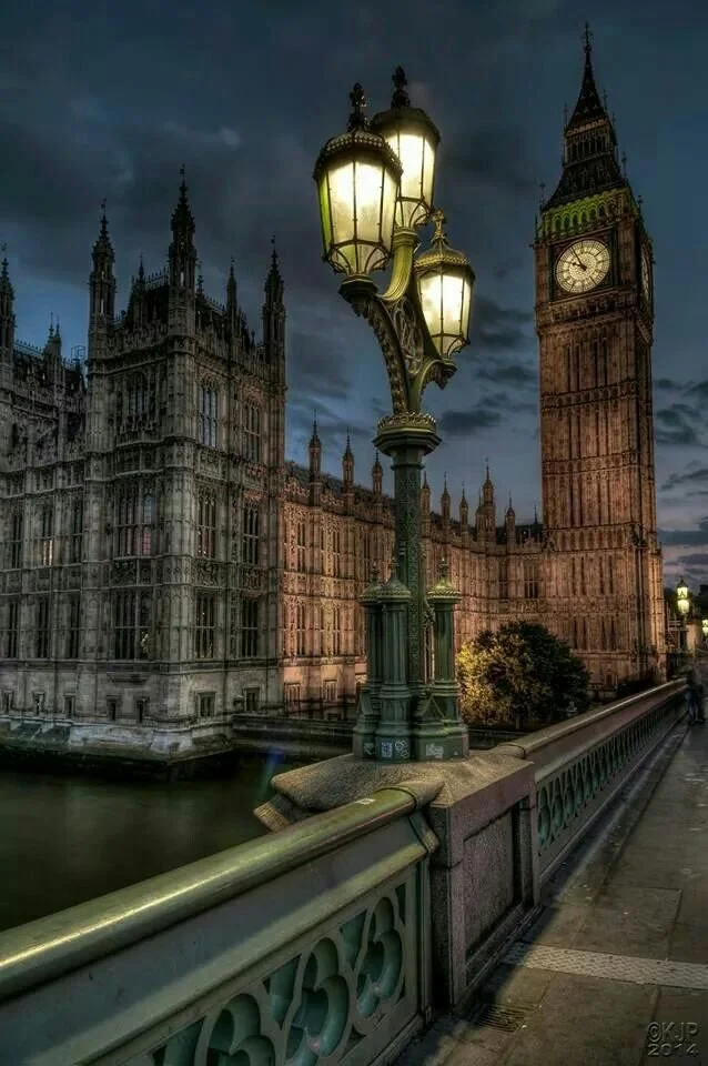 Nighttime view of Big Ben and the Houses of Parliament in London, with a lit street lamp on Westminster Bridge.