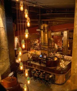 Interior of a bar or restaurant with warm lighting, hanging pendant lights, a curved bar counter, and barstools, creating an inviting atmosphere.