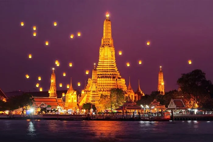 Nighttime view of a lit temple with floating lanterns in the sky over a body of water