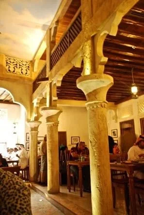 Interior of a restaurant with large stone columns, wooden ceiling beams, and people dining at tables.