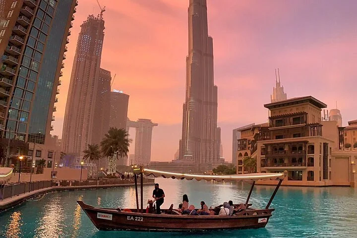 People on a boat in a waterway with the Dubai skyscraper in the background at sunset.