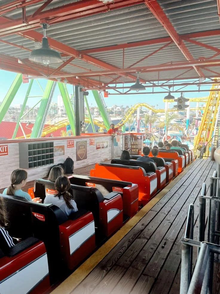 People riding a roller coaster at an amusement park, with visible green and yellow roller coaster tracks and a sunny day.