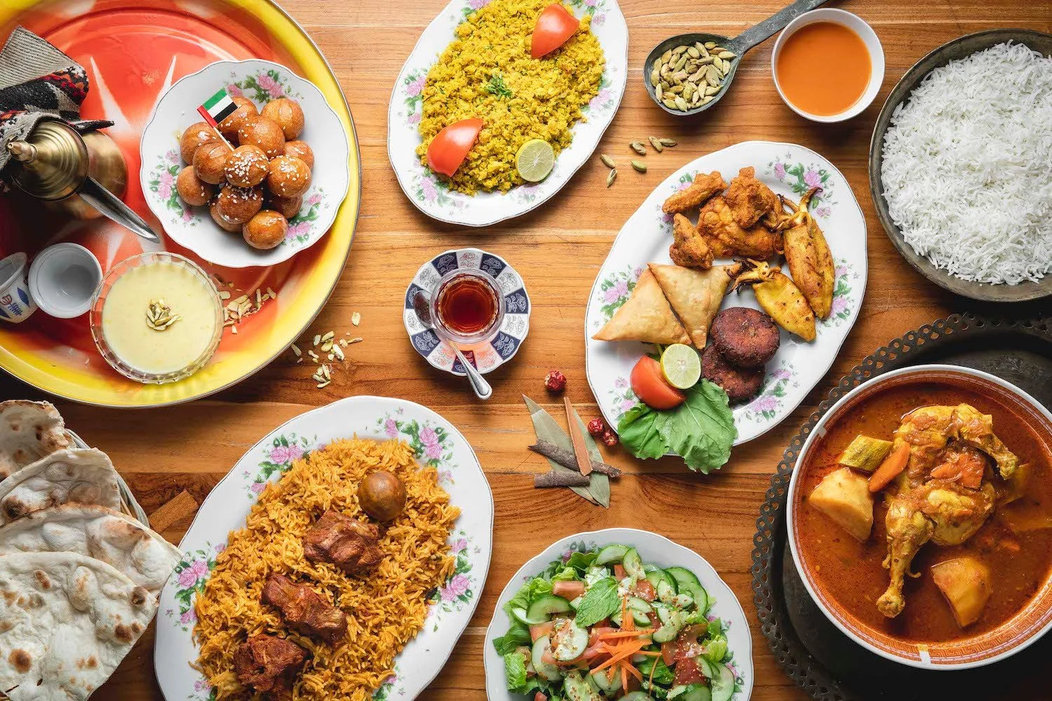 A variety of Indian dishes on a wooden table, including rice, curry, salad, fried snacks, and sweets.