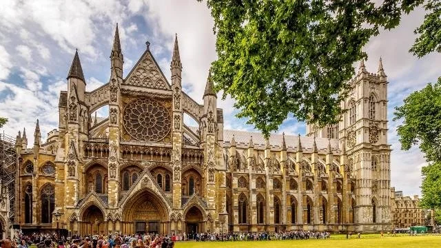 Gothic cathedral with intricate stonework and stained glass windows, surrounded by trees and a crowd of tourists