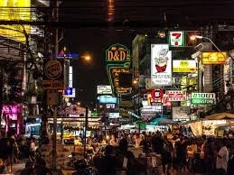 Nighttime busy street market with numerous illuminated signs and storefronts.