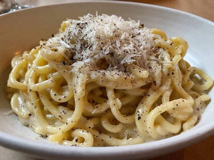 A bowl of cooked spaghetti pasta topped with grated cheese and black pepper.