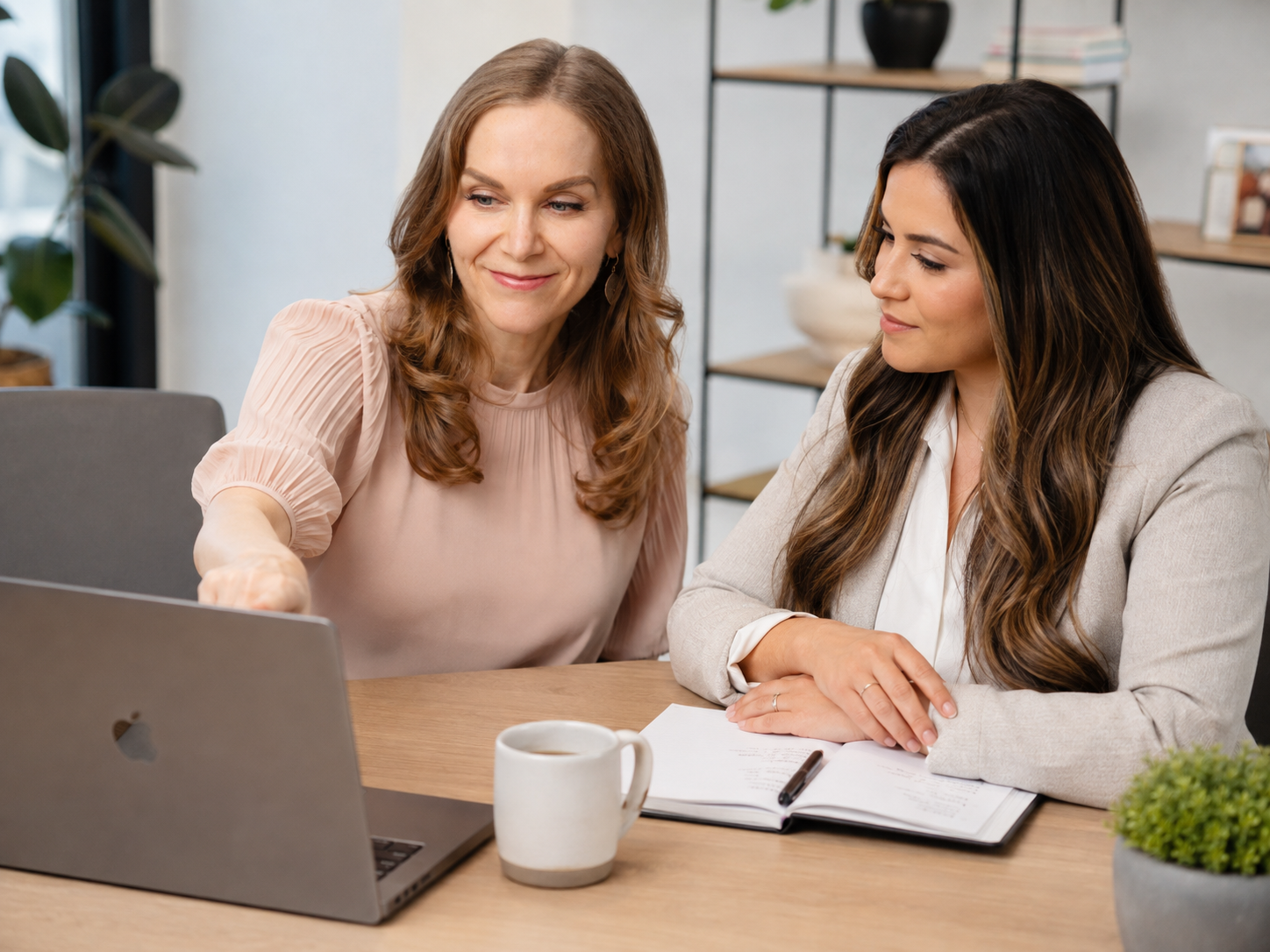Susan Hovey, Founder of SMASH Marketing & Success Coaching, sits with a female client at a desk, looking at a laptop, with notebooks and a coffee mug in front of them, discussing marketing strategy one-on-one.