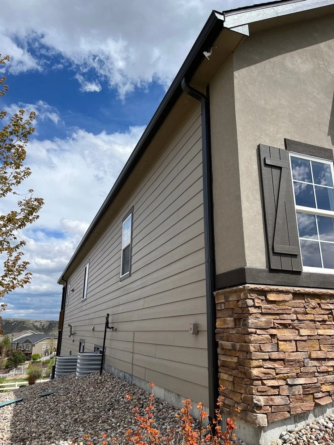 Brown seamless gutter installed along the roofline of a tan-sided home with stone accents.